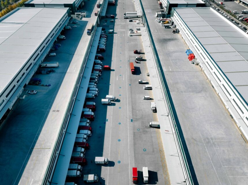 Aerial view of trucks outside giant logistics warehouse transit centre.