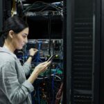 IT professional using a mobile device while working with network equipment in a server room.