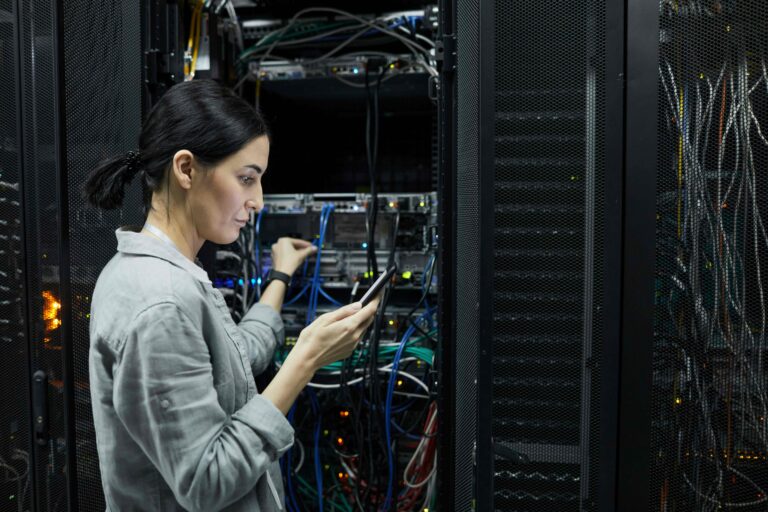 IT professional using a mobile device while working with network equipment in a server room.