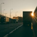 A delivery truck drives down a highway with the sunset ahead.