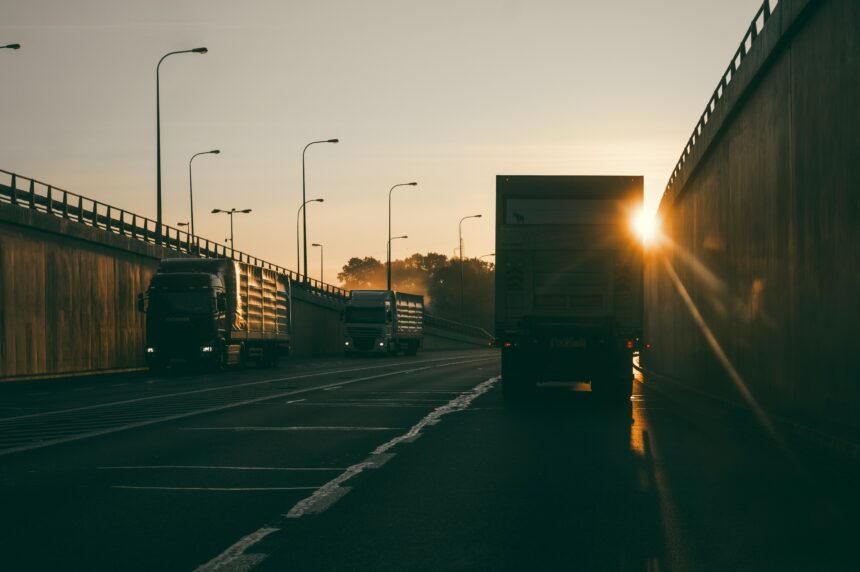 A delivery truck drives down a highway with the sunset ahead.