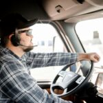 A man is driving a truck wearing a hands-free headset.