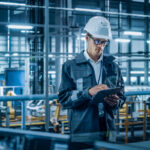 A man uses handheld device while standing in a warehouse environment.