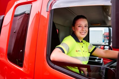 Australia Post worker in high-visibility clothing sitting in the driver’s seat of a red delivery truck.