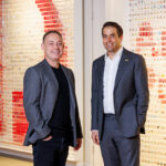 Two men in suits stand in front of the Australia Post logo.