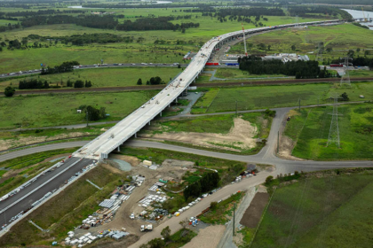 Aerial view of a major motorway extension under construction, crossing green farmland and waterways.