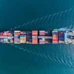 Aerial view of a large cargo ship carrying colourful shipping containers across blue ocean waters, illustrating maritime freight and global trade.