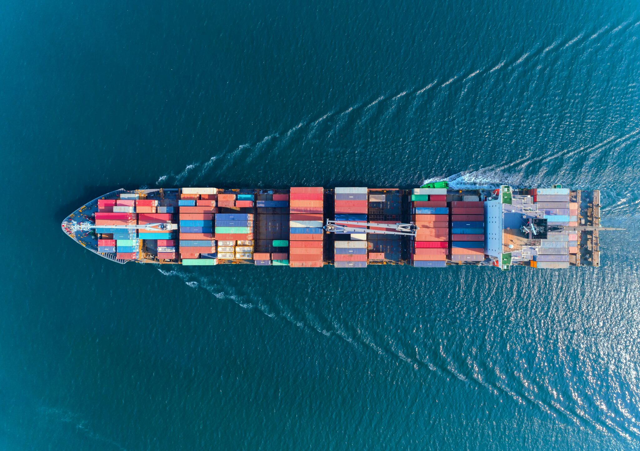 Aerial view of a large cargo ship carrying colourful shipping containers across blue ocean waters, illustrating maritime freight and global trade.