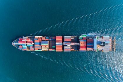 Aerial view of a large cargo ship carrying colourful shipping containers across blue ocean waters, illustrating maritime freight and global trade.