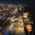 Cargo ship at the dock at night surrounded by hundreds of shipping containers.
