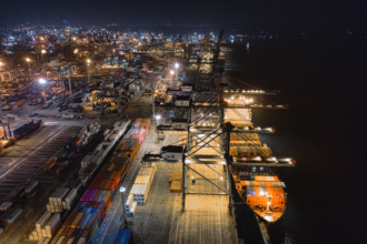 Cargo ship at the dock at night surrounded by hundreds of shipping containers.
