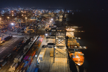 Cargo ship at the dock at night surrounded by hundreds of shipping containers.