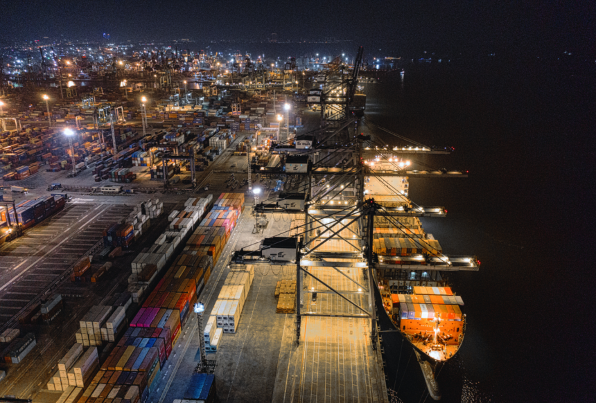 Cargo ship at the dock at night surrounded by hundreds of shipping containers.