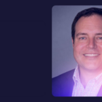 Professional headshot of a smiling man wearing a dark blazer and checked shirt, featured in a TMX-branded graphic with a navy background and pink and purple gradient.