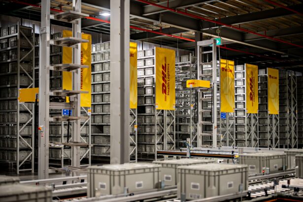 Automated warehouse storage and conveyor systems at a DHL Health Logistics facility, featuring high-density shelving, grey storage containers and DHL-branded signage.