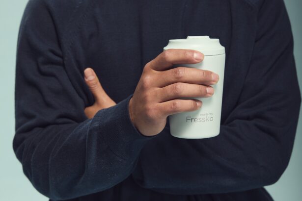 Person wearing a navy jumper holding a light grey made by Fressko reusable coffee cup, with the brand's logo visible on the front.