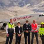 Qantas Freight and Australia Post representatives standing alongside pilots and ground crew in front of an Australia Post-branded Airbus A321 freighter aircraft.